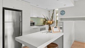 A modern kitchen with stainless steel appliances, a white countertop, and a bar area with stools. - A Touch Of Class (Lorne)