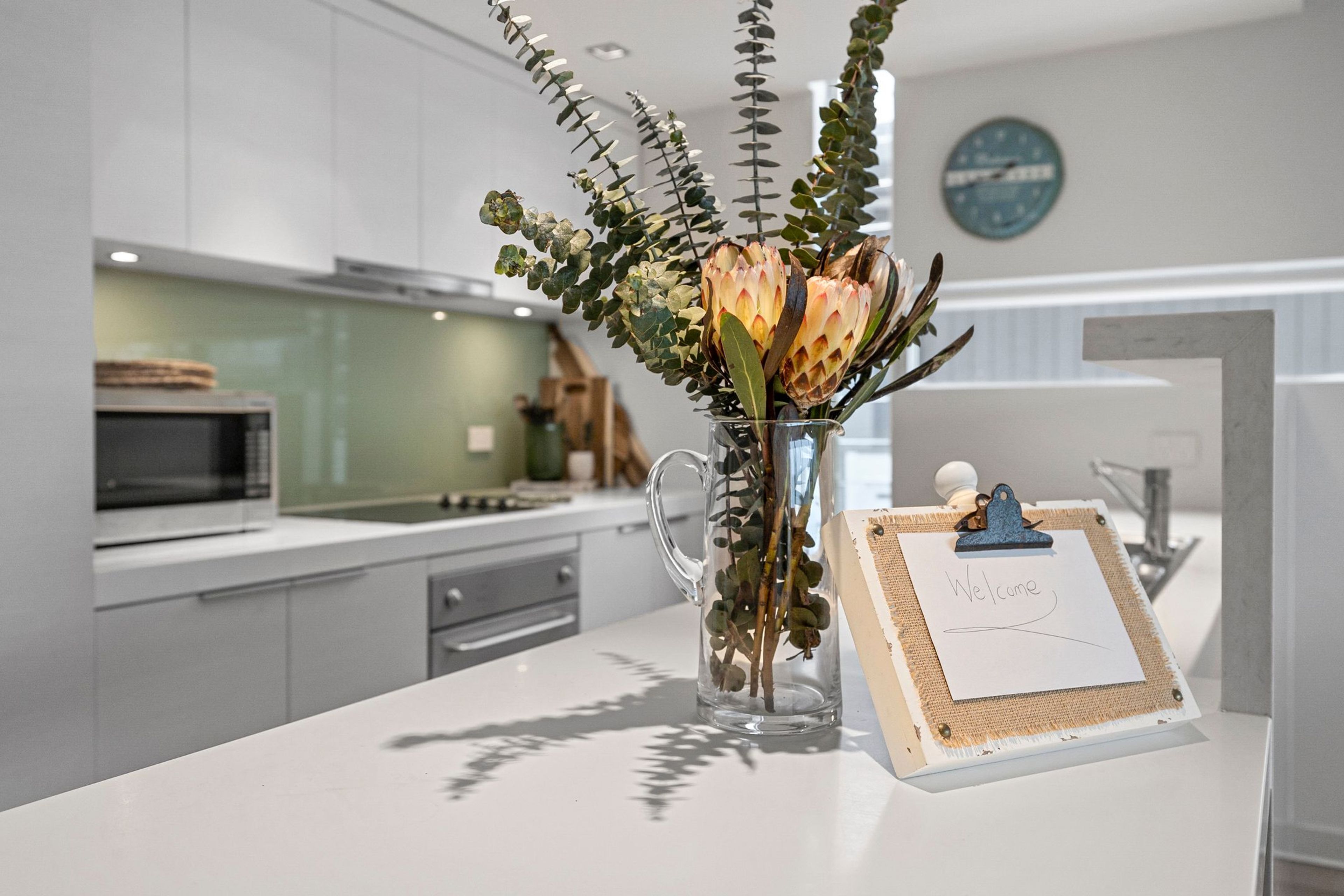 Une cuisine moderne avec un vase en verre transparent contenant des fleurs, posé sur un comptoir blanc.