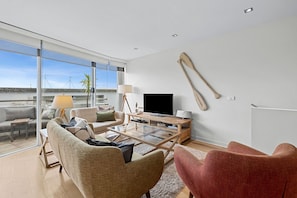 A modern living room with a large glass door leading to a balcony, a flat-screen TV, and a wooden coffee table. - A Touch Of Class (Lorne)