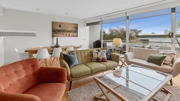 A modern living room with a glass coffee table, sofas, and a dining area with chairs. - A Touch Of Class (Lorne)