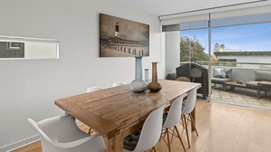 A dining area with a wooden table, white chairs, and a painting of a lighthouse. - A Touch Of Class (Lorne)