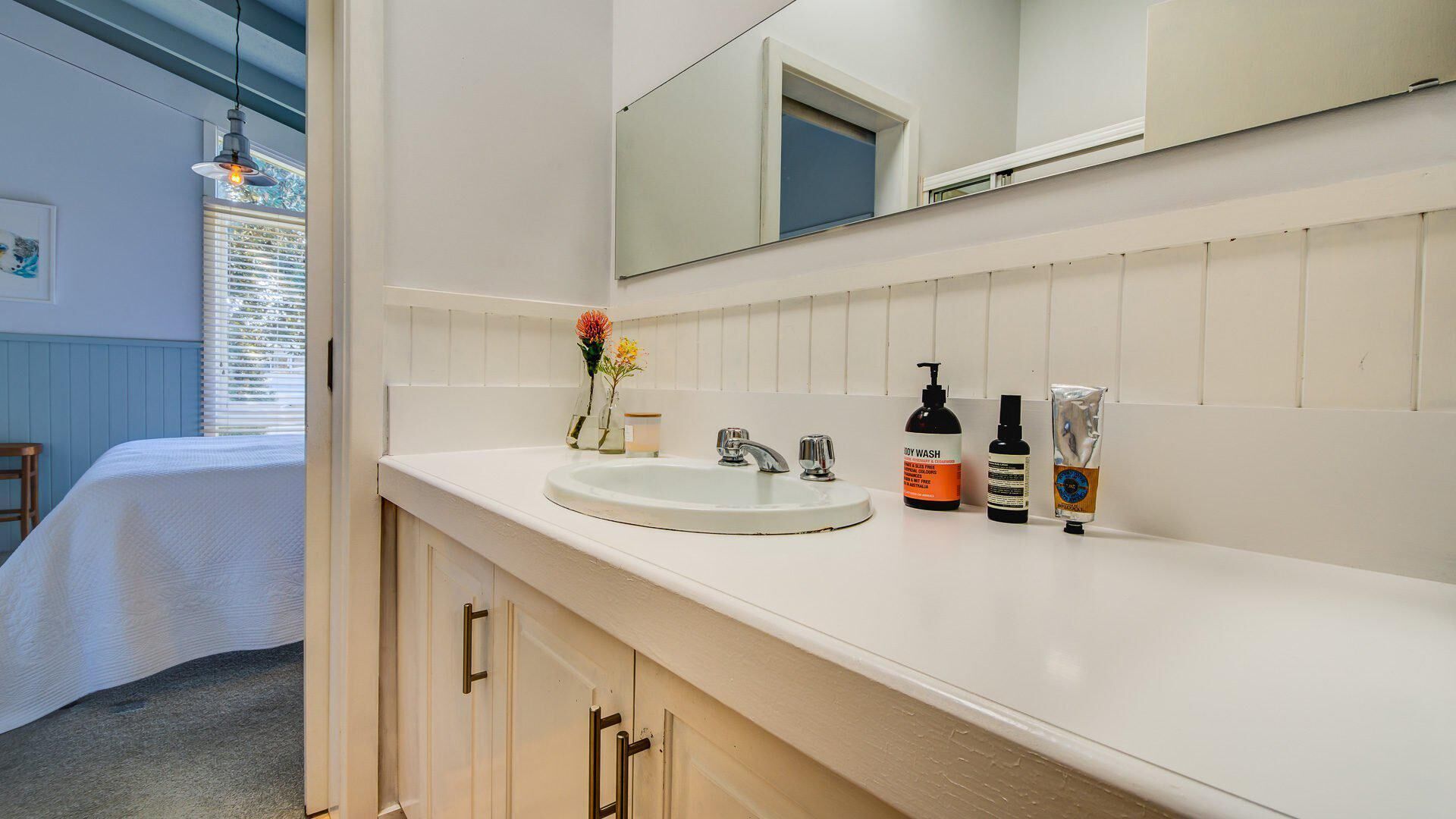 Une salle de bain avec un lavabo blanc, deux robinets, un miroir et des articles de toilette posés sur le comptoir.