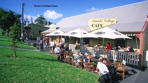 An outdoor cafe with wooden tables and chairs, a fenced patio area, and a sign for 'Amaki Cottage Cafe'. - Blue Waves, Kiama, South Coast (Kiama)