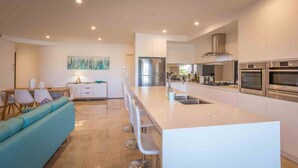 A modern kitchen with a central island, stainless steel appliances, and a dining area with a sofa and chairs. - Blue Waves, Kiama, South Coast (Kiama)
