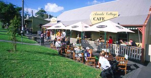 An outdoor cafe with wooden tables and chairs, a fenced patio area, and a sign for 'Amaki Cottage Cafe'.