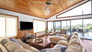 Un salón espacioso con techo de madera, ventanas grandes, televisor de pantalla plana y asientos cómodos.