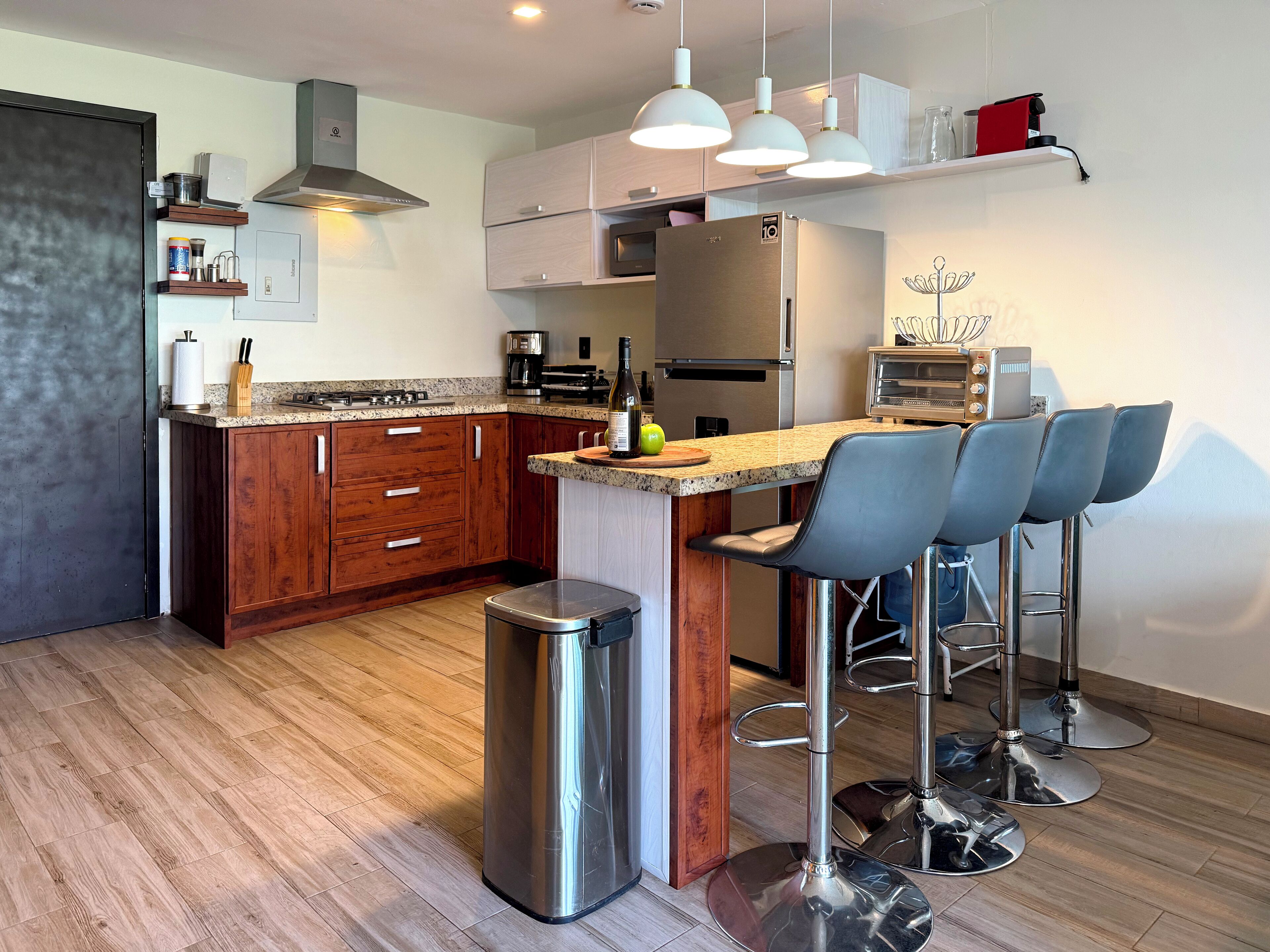 A modern kitchen with wooden cabinets, a stainless steel refrigerator, a built-in oven, and a bar area with bar stools.