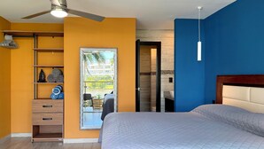 Quarto com cama, ventilador de teto, janela com vista e banheiro visível por uma porta aberta.