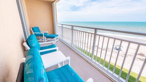 A balcony with white chairs and a table, overlooking a beach with a railing. - Oceanfront 2BR Condo 3rd Floor Balcony Views, Unit 307 (Indian Harbour Beach)