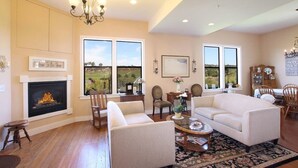 A spacious living room with a fireplace, comfortable seating, and large windows offering a view of the outdoors.