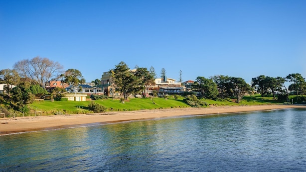 A riverside view with a sandy beach, grassy areas, and buildings in the background.