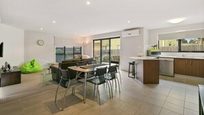 A modern kitchen with a dining area, a green bean bag chair, and a large window overlooking a garden.
