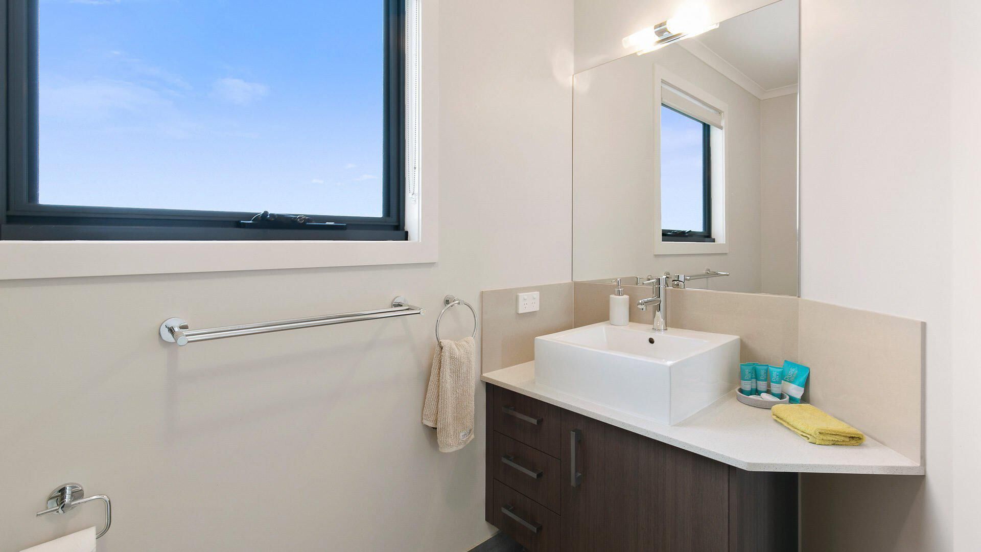 A modern bathroom with a large window, a white sink, dark wooden cabinets, and a towel rack.