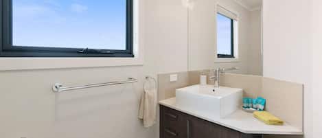 A modern bathroom with a large window, a white sink, dark wooden cabinets, and a towel rack.