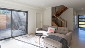 A modern living room with a sofa, a coffee table, and a staircase leading to an upper floor. - Coastline, Boat Harbour - Gerringong (Gerringong)