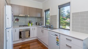 A modern kitchen with white cabinets, a stainless steel range hood, a built-in oven, a dishwasher, and a window providing a view of the outdoors. - Coastline, Boat Harbour - Gerringong (Gerringong)