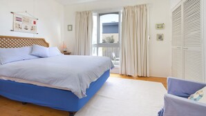 A bedroom with a large bed, a chair, a window with curtains, and a wall with a framed picture. - HOME SWEET HOME - MOUNT MARTHA (Mount Martha)