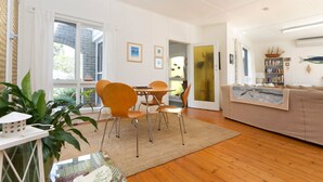 A modern living room with a wooden floor, a beige sofa, a dining table with chairs, and a bookshelf. - HOME SWEET HOME - MOUNT MARTHA (Mount Martha)