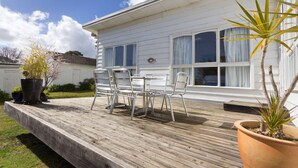 A wooden deck with metal chairs and a table, a white house with large windows, and potted plants. - HOME SWEET HOME - MOUNT MARTHA (Mount Martha)