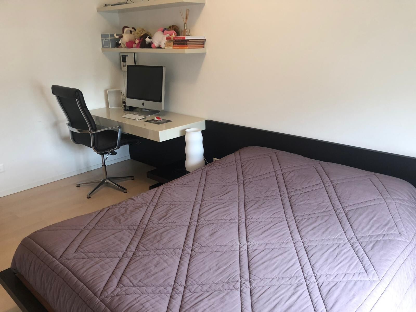 Ein Schlafzimmer mit einem Bett, einem Schreibtisch inklusive Computer, einem Sessel und einem Regal mit Dekoration.