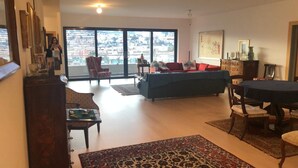 Amplia sala de estar con un ventanal, un sofá azul, una mesa de comedor y un tapete estampado.