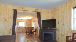 A wooden-paneled room with a fireplace, a television, a dining table with chairs, and a sofa.