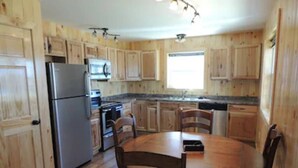 A kitchen with wooden cabinets, a stainless steel refrigerator, a stove, and a dining table with chairs.