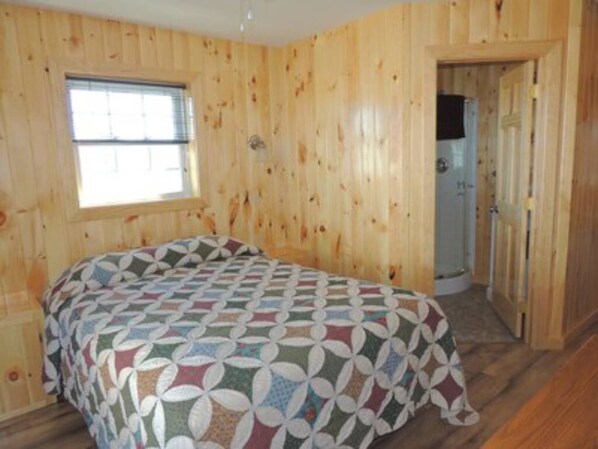 Una habitación de cabaña de madera con cama, ventana y puerta.