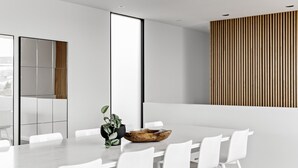 Ein moderner Besprechungsraum mit großem Tisch, weißen Stühlen, einer Holbschale als Mittelpunkt und einer vertikalen Holzverkleidung an der Wand.