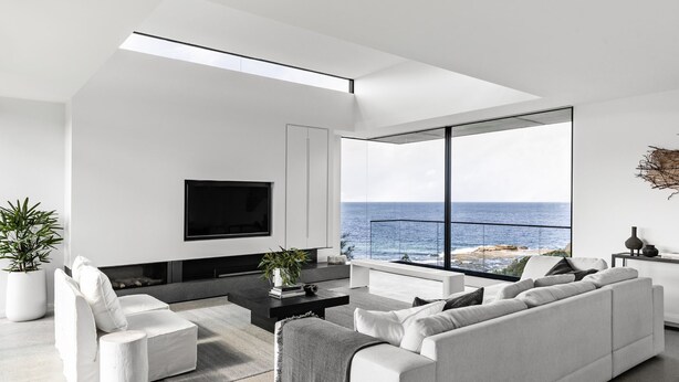 Ein modernes Wohnzimmer mit großem Fernseher, weißen Möbeln und Blick auf den Ozean.
