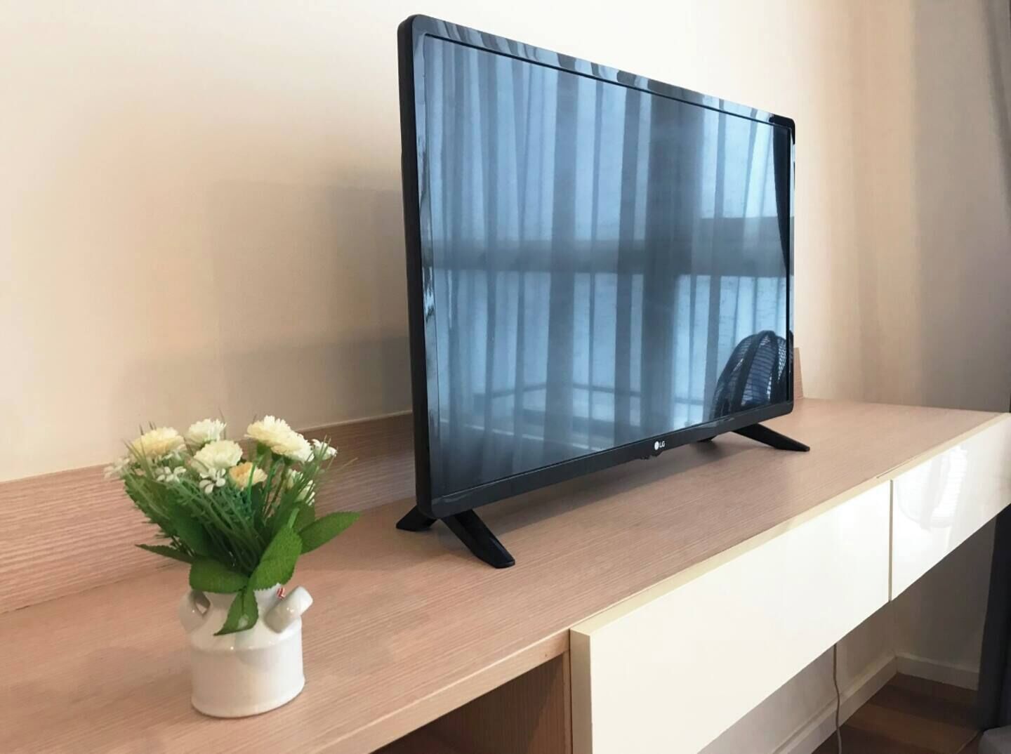A flat-screen TV on a wooden desk with a white cabinet underneath.