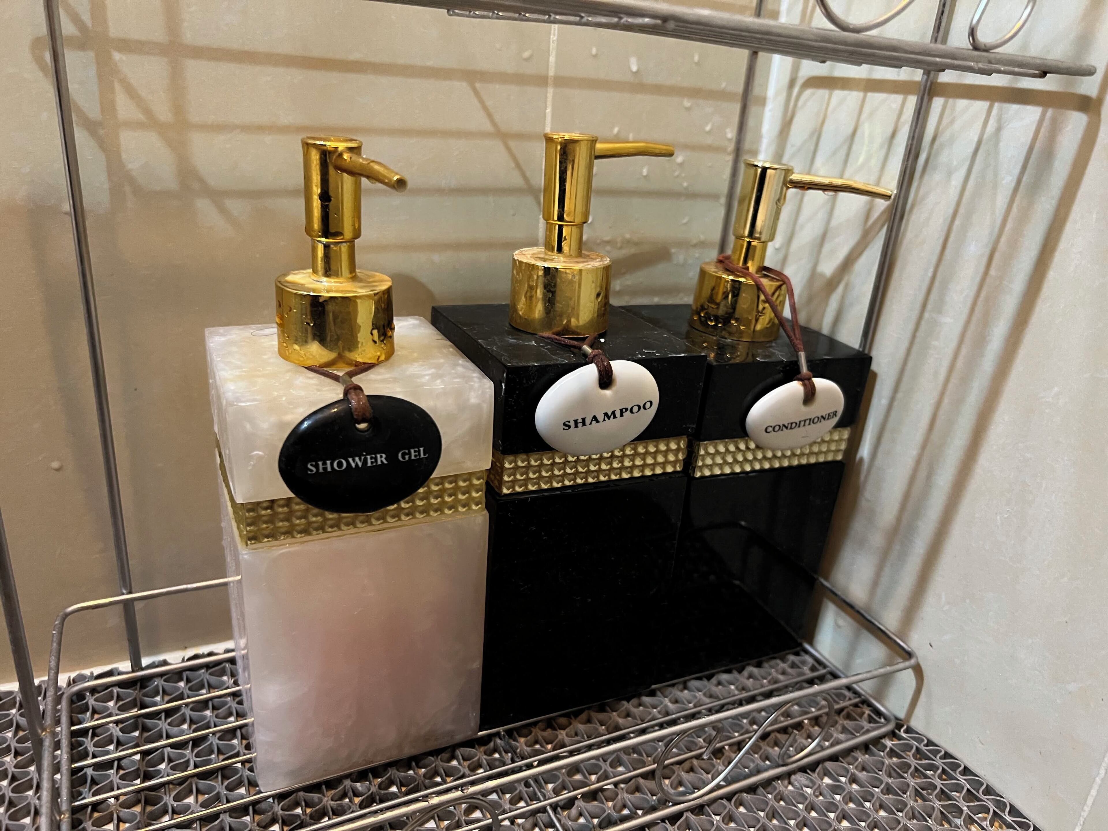 Ein Badezimmer mit drei Waschbecken, jedes beschriftet mit einem anderen Produkt: Duschgel, Shampoo und Conditioner.