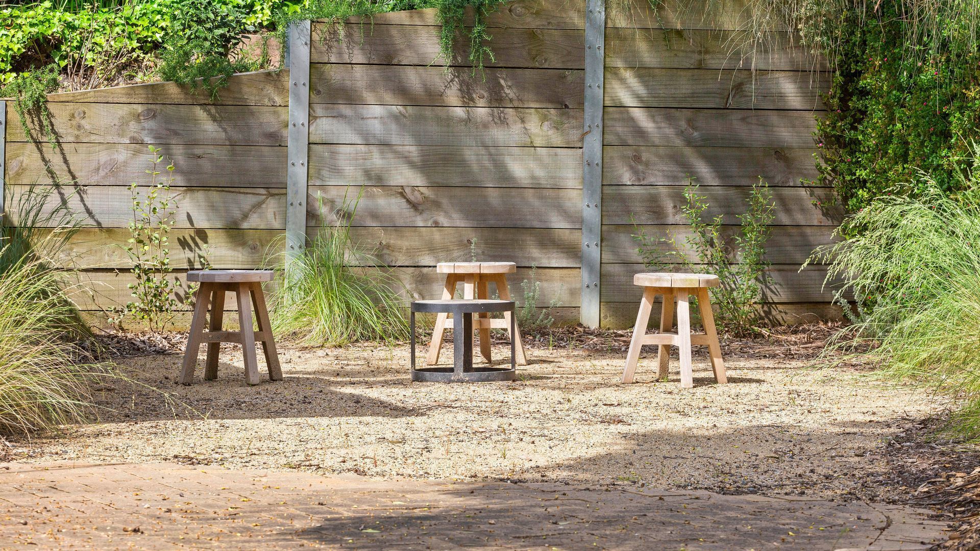 Three wooden stools arranged on a gravel path with a wooden fence in the background.