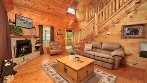 Ein Interieur einer Holzhütte mit Kamin, einer Couch, einem Couchtisch und einer Treppe.