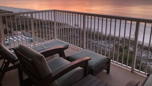 A balcony with two wooden chairs and a table, overlooking a beach with a sunset view. - 🏖Beachfront Retreat on Perdido Key. Two Pools, Hot Tub, and Gym🏖 (Perdido Key)