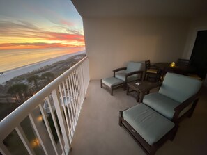 Un balcón con vista a la playa al atardecer, amueblado con dos sillones y una mesita.