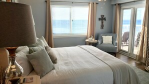 A bedroom with a bed, a side table, a lamp, a chair, and a view of the outdoors through a sliding door. - 🏖Beachfront Retreat on Perdido Key. Two Pools, Hot Tub, and Gym🏖 (Perdido Key)
