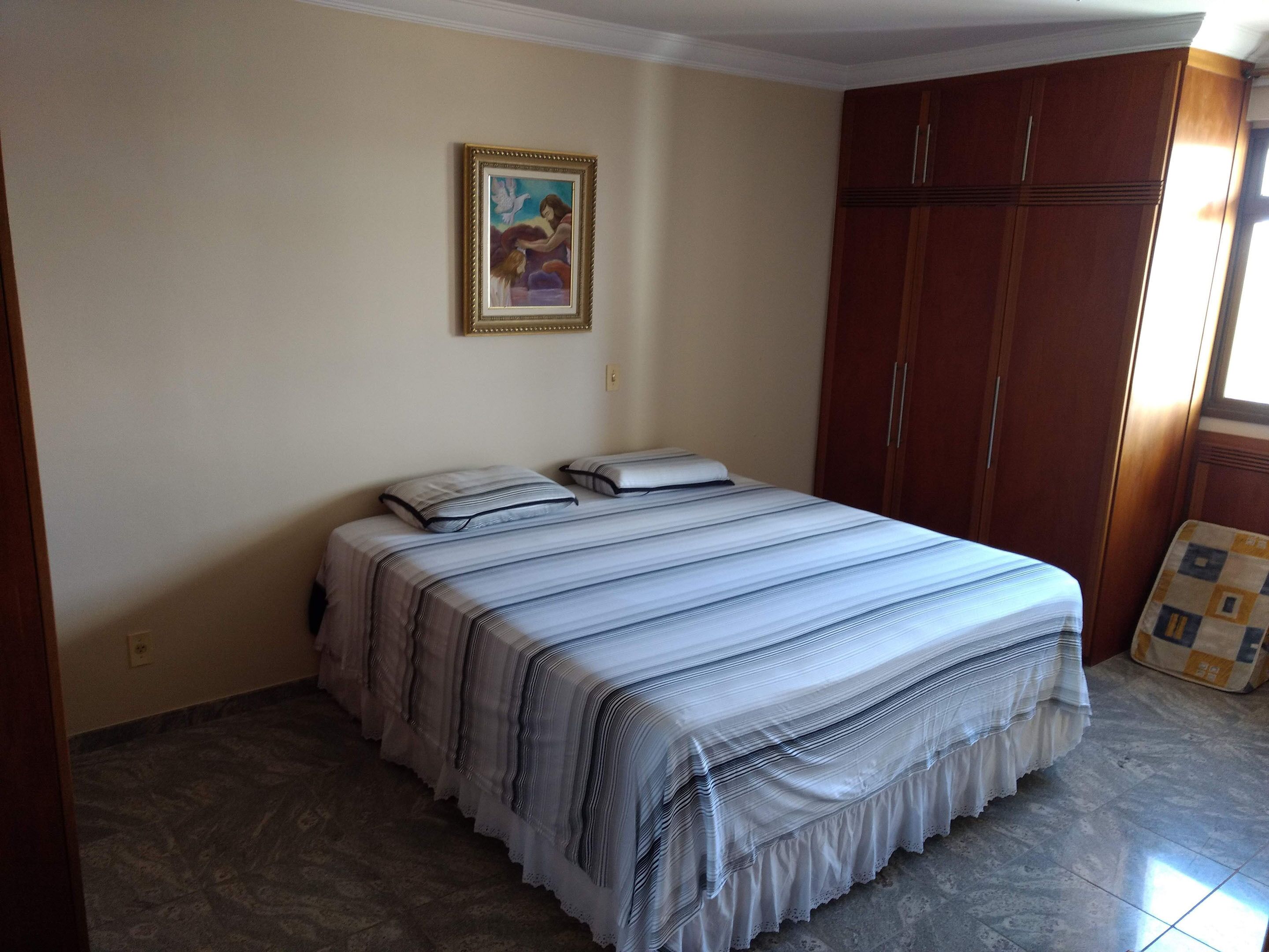 A bedroom with a bed, a framed picture on the wall, and a wardrobe.
