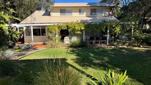 A two-story house with a covered porch, a lawn, and a garden with various plants and a small pond.