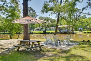 A picnic setup with a table and chairs near a lake, surrounded by trees and a house in the background. - Waterfront Foley Area Home - 15 Mi to Gulf! (Elberta)