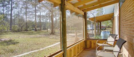 A covered porch with wooden railings, a brick wall, and a view of a grassy area with trees.
