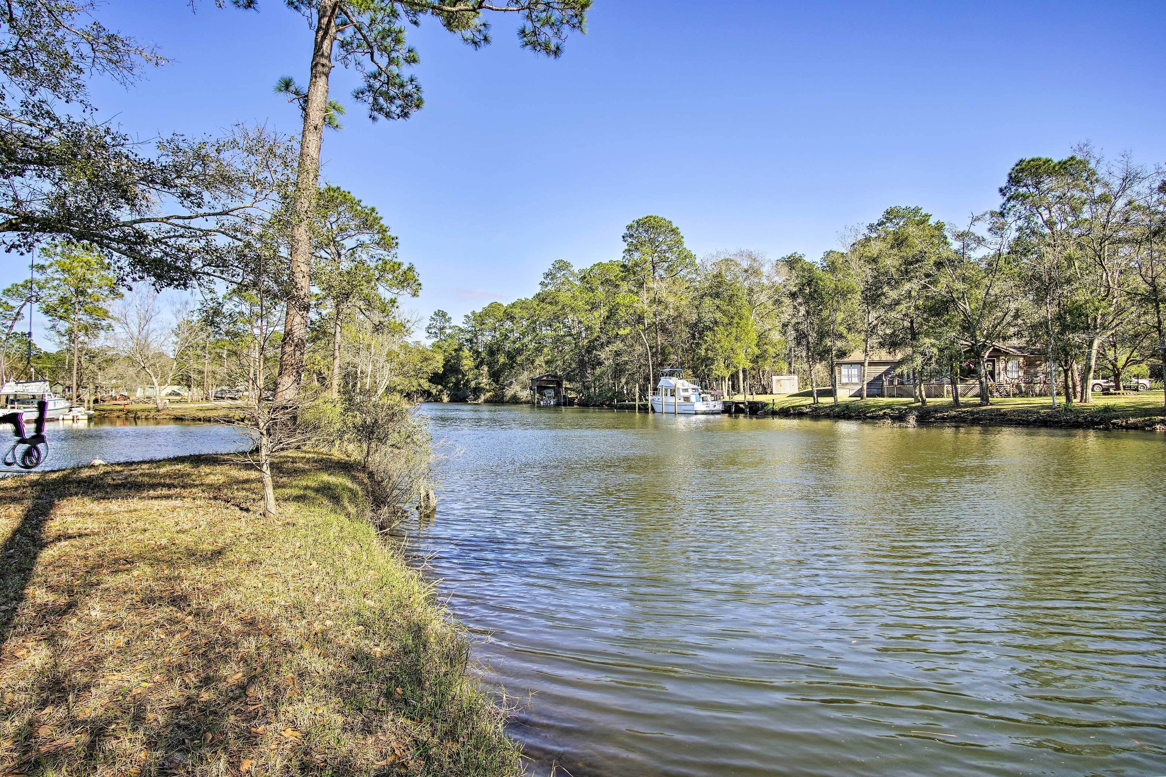 A calm river with a boat docked on the right, surrounded by trees and a grassy area.