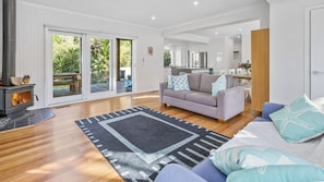 Cozy living space with a fireplace, sofa, and dining area, leading to a patio with lush greenery.