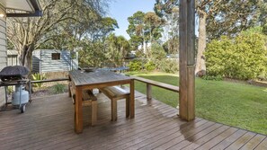 Enjoy dining or relaxation on the deck with a wooden table and benches, surrounded by a well-maintained lawn and lush greenery.