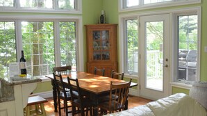 Uma sala de jantar com mesa e cadeiras de madeira, sofá branco e um armário com portas de vidro.