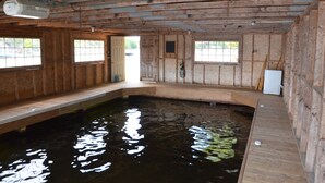 Interior em madeira com uma grande piscina retangular, paredes de madeira e uma porta que dá para o exterior.