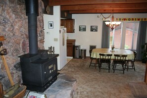 Cozy living space with a traditional stove, dining area, and kitchen, featuring a rustic charm and a window with a view.