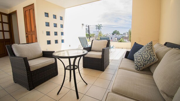 Een balkon met rieten meubels, een glazen tafel en een bank met kussens.