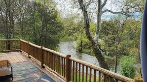 Eine Holzterrasse mit Geländer, mit Blick auf einen Fluss und Wald.