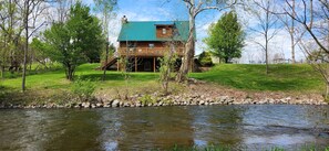 Une cabane en rondins avec un toit végétalisé, une véranda et une rivière en contrebas.